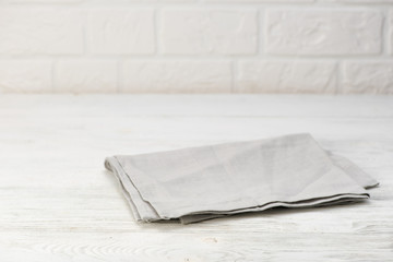 Gray napkin isolated on white wooden table. Copy space. Brick wall background. Front view.