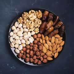 Assorted nuts, almonds, pistachios, walnuts, hazelnuts and figs on a black ceramic plate   dark background. Top view