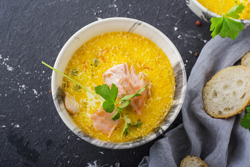 Intense fragrant homemade thick rich soup with salmon in a la carte dishes against  dark background. Top view
