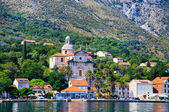 Waterfront of small town Prcanj along Bay of Kotor, Montenegro. View of Birth of Our Lady Church, coastal villas, gardens and mountain from sea.