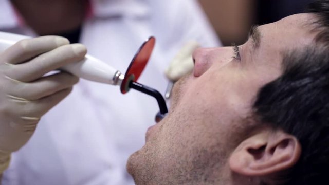 Dentist working with dental polymerization lamp in oral cavity.