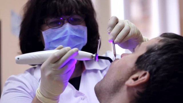 Dentist working with dental polymerization lamp in oral cavity.