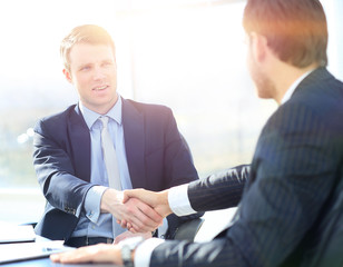 Business colleagues sitting at a table during a meeting with two male executives shaking hands