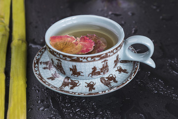 Cup of flower tea and bamboo stems with water drops on black slate