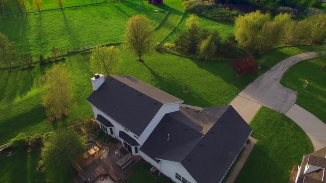 Evening aerial flyby of scenic rural home surrounded by trees in Springtime.
