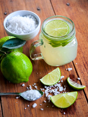 Lemonade in jar with fresh lime slice and sea salt on wooden table.