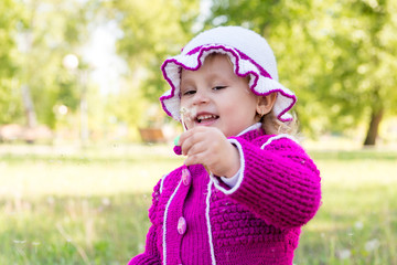 The child, a little girl blowing on a dandelion. Walk through the park in spring. Carefree childhood.