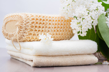 Fototapeta na wymiar Махровые полотенца, мочалка и белая сирень на столе