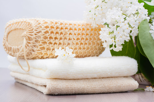 Махровые полотенца, мочалка и белая сирень на столе