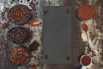 Different type of coffee, chocolate and spices on rustic table with slate blackboard 