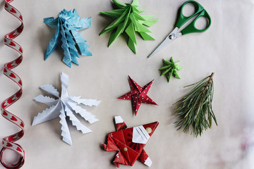 Overhead of Handmade origami Christmas ornaments, ribbon and scissors on paper background. Subject...