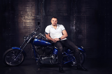 Fashion portrait of a handsome young athletic man sitting on a shiny cool motorbike in his garage