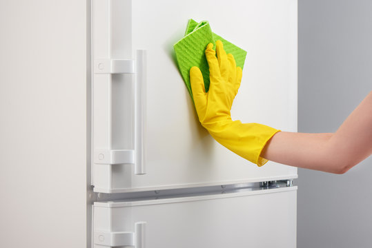 Hand in yellow glove cleaning white refrigerator with green rag