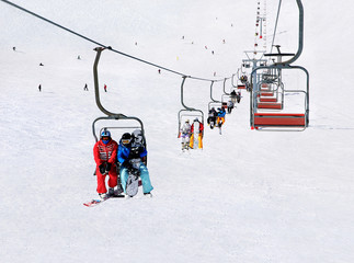 Chairlift (ski lift) transport skiers and snowboarders up a snowy downhill at winter ski snow...