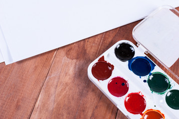 Paper and watercolor paints on the wooden background
