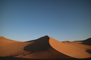 Fototapeta na wymiar Deserto com grande duna em formato de pico em destaque, sombras projetadas na areia e céu azul