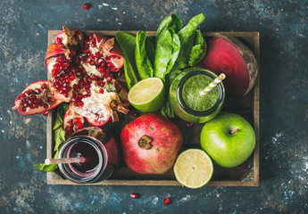 Green and purple fresh juices or smoothies with fruit, greens, vegetables in wooden tray, top view,...