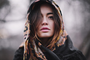 Attractive, charming young woman in a colored scarf in Russian style walking in the autumn park....