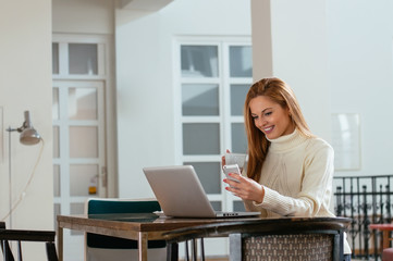 An attractive young businesswoman using her phone and laptop at