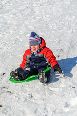 Fototapeta na wymiar Little boy enjoying a sleigh ride. Children play outdoors in sno