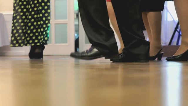 Women and men dancing at a wedding indoors. People's feet close up