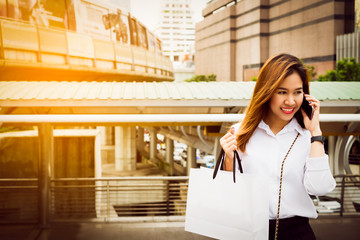 Charming beautiful woman using smartphone and handle paper shopping bag with city background. lifestyle in city