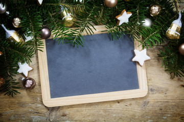 Slate writing board with fir tree branches, christmas balls and cookies on rustic wood, holiday background