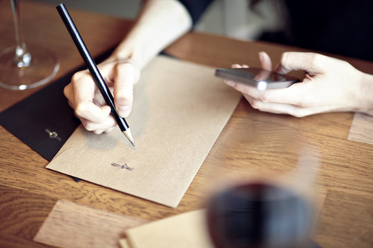 Having lunch with red wine in a cafe or restaurant. Hipster lifestyle. Blank paper envelope, phone. wooden table