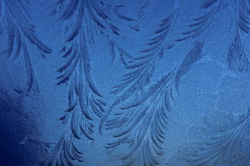Ice formations on glass with smooth delicate patterns in blue tones