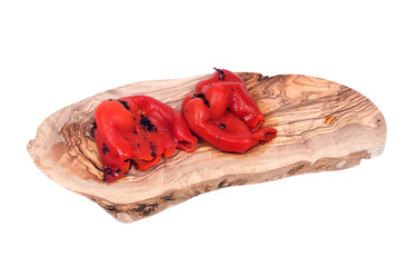 Fire roasted red peppers on olive wood cutting board isolated on white background