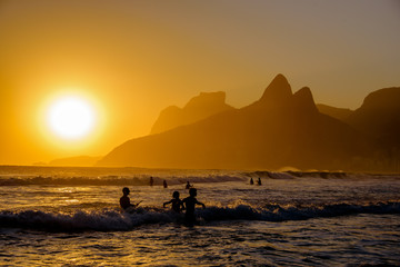 Unidentifiable silhouettes enjoying late afternoon sun rays on Ipanema beach in Rio de Janeiro,...