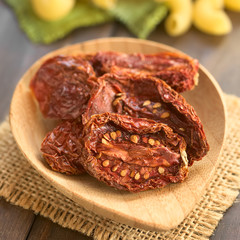 Sun-dried tomato halves on bamboo plate, photographed with natural light (Selective Focus, Focus in the middle of the first tomato half)