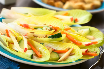 Fresh salad of endive leaves, cucumber, carrot, apple and sunflower seeds, photographed with natural light (Selective Focus, Focus in the middle of the image)