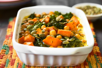 Baked pumpkin, kale and chickpea casserole with pumpkin seeds on top in casserole dish,...