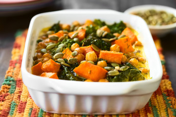 Baked pumpkin, kale and chickpea casserole with pumpkin seeds on top in casserole dish, photographed with natural light (Selective Focus, Focus one third into the dish)
