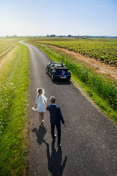 Top view. Newlyweds walking on a country road to their car.