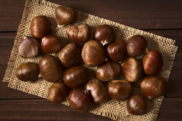 Fresh raw chestnuts, photographed overhead on wood with natural light (Selective Focus, Focus on the top of the chestnuts)