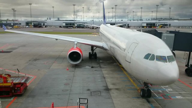 Passenger airplane docked at the gate at boarding time, engine fan blades slowly spinning, clouds passing on high winds in the background. No logos or people.