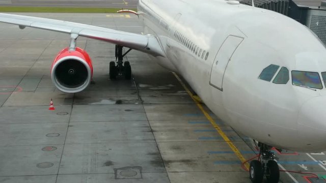 Airplane idling during boarding at airport gate, pan starting from cockpit over the engine to the tip of the wing, no logos, no people