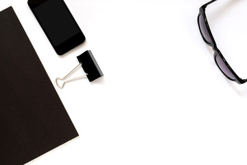 Flat lay photo of office desk with black book, smartphone, eyeglasses and paper clip with copy space background