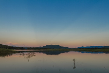 Sunset in twilight time behind the mountains front water of a reservoir with copy space.
