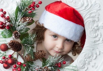 little curly child in santa hat with Christmas decorations