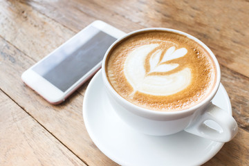 Cup of coffee with heart pattern in a white cup on wooden backgr