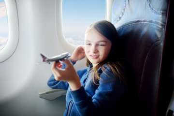 Adorable little girl traveling by an airplane. Child sitting by the window and playing with toy plane.