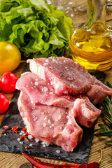Raw pork steaks on stone board with herbs, tomatoes and lemon.