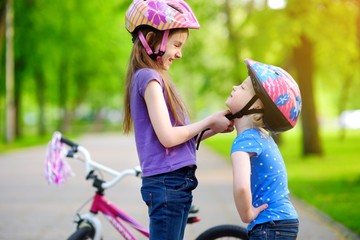 Adorable girl helping her sister to put a bicycle helmet on