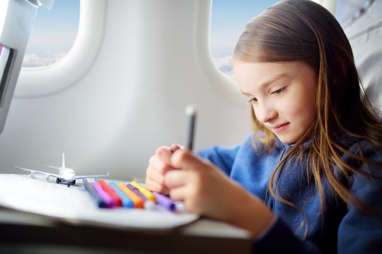 Adorable little girl traveling by an airplane. Child sitting by the window and drawing.