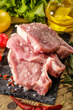 Raw pork steaks on stone board with herbs, tomatoes and lemon.