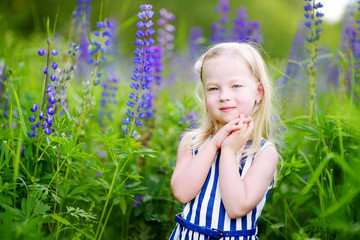 Cute little preschooler girl having fun in beautiful blooming lupine field