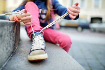 Cute little girl learning to tie shoelaces outdoors - obrazy, fototapety, plakaty